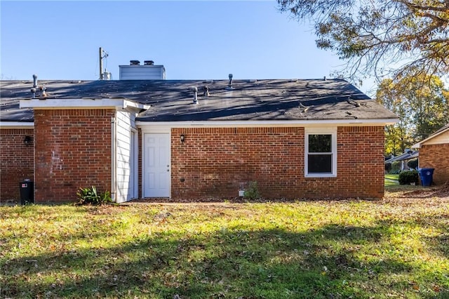 back of house featuring brick siding, a chimney, and a lawn