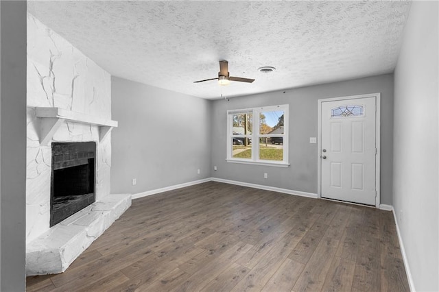 unfurnished living room with baseboards, a fireplace, a textured ceiling, a ceiling fan, and dark wood-style flooring