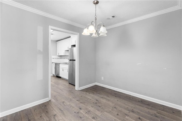 unfurnished dining area featuring visible vents, wood finished floors, an inviting chandelier, crown molding, and baseboards