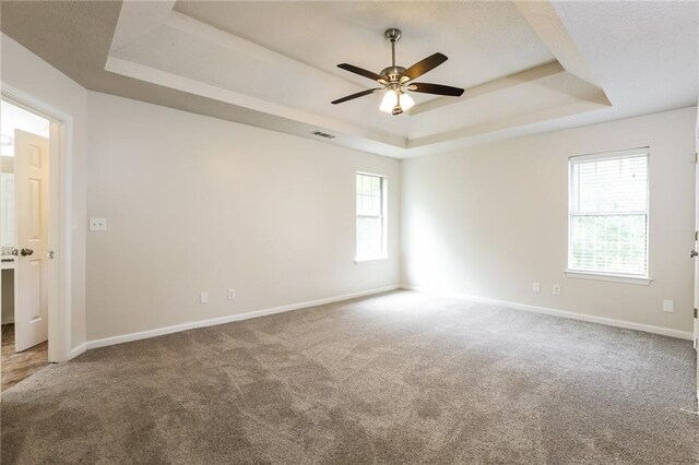 carpeted spare room with ceiling fan and a raised ceiling