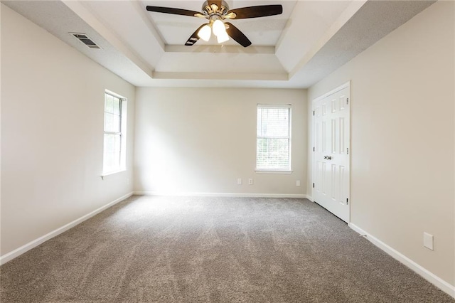 carpeted spare room featuring ceiling fan and a raised ceiling