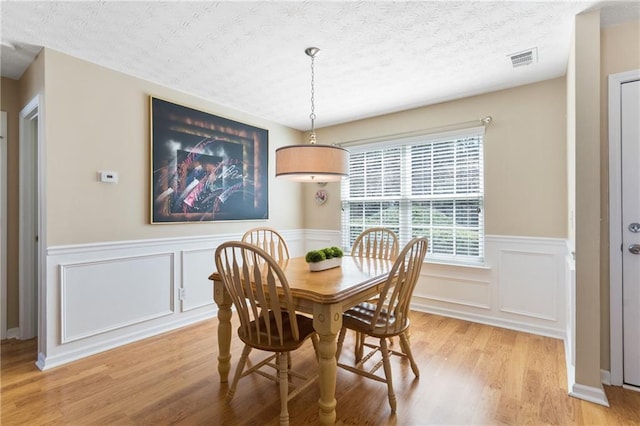 dining space featuring visible vents, wainscoting, a textured ceiling, and light wood-type flooring