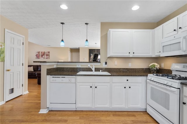 kitchen with white appliances, a peninsula, a sink, white cabinets, and decorative light fixtures