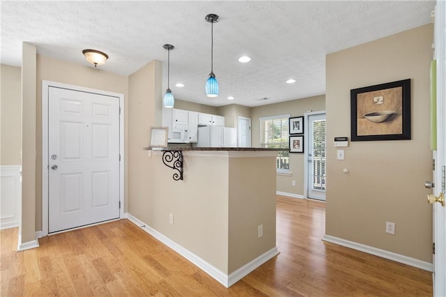 kitchen with light wood-style flooring, dark countertops, white cabinetry, white appliances, and a peninsula