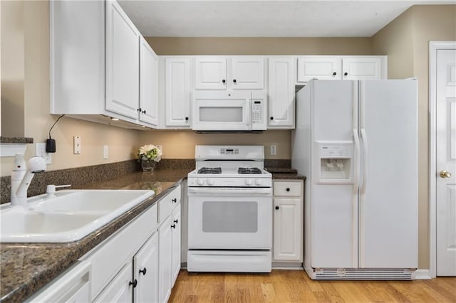 kitchen with dark stone counters, light wood-type flooring, white cabinets, white appliances, and a sink