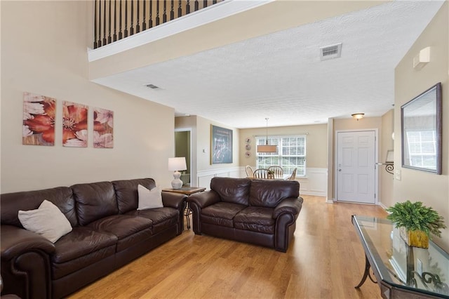 living room featuring a wainscoted wall, visible vents, light wood-type flooring, and a textured ceiling