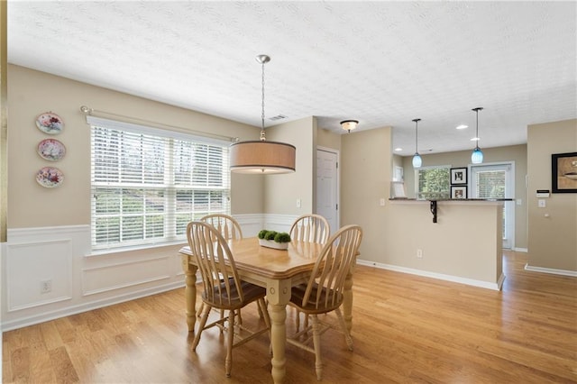 dining space with wainscoting, visible vents, light wood-style flooring, and a textured ceiling