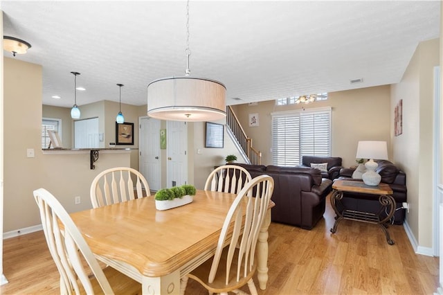 dining space with stairway, light wood-style floors, visible vents, and baseboards