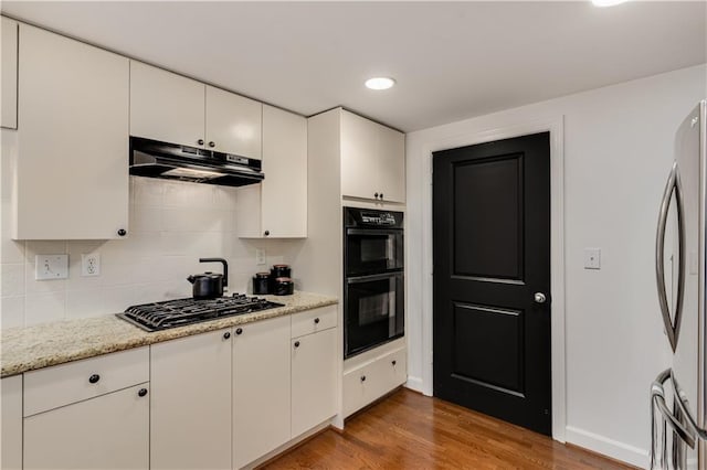 kitchen with black appliances, under cabinet range hood, wood finished floors, white cabinets, and decorative backsplash