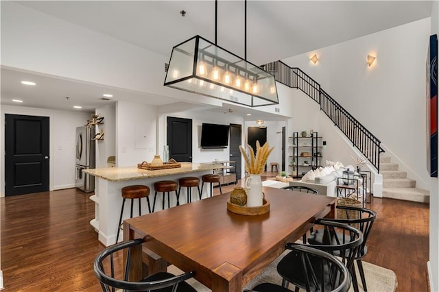 dining space featuring dark wood-type flooring, baseboards, stairway, recessed lighting, and a towering ceiling