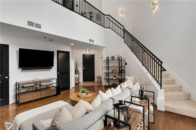 living room featuring stairs, wood finished floors, visible vents, and a towering ceiling