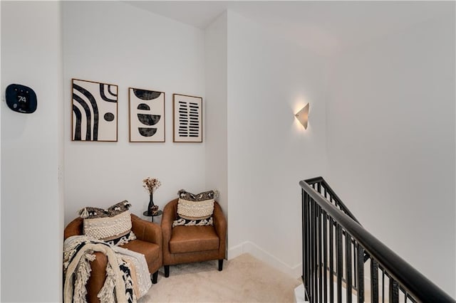 living area with baseboards, light carpet, and an upstairs landing