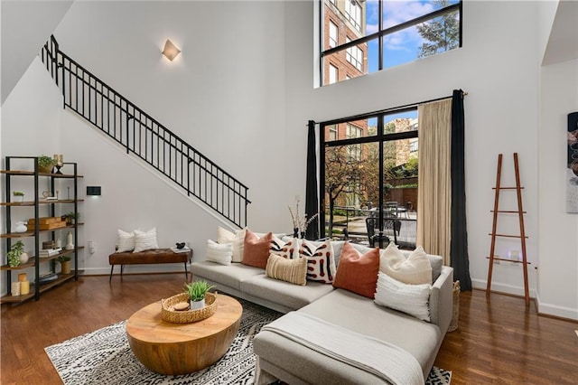 living area with stairway, a high ceiling, baseboards, and wood finished floors