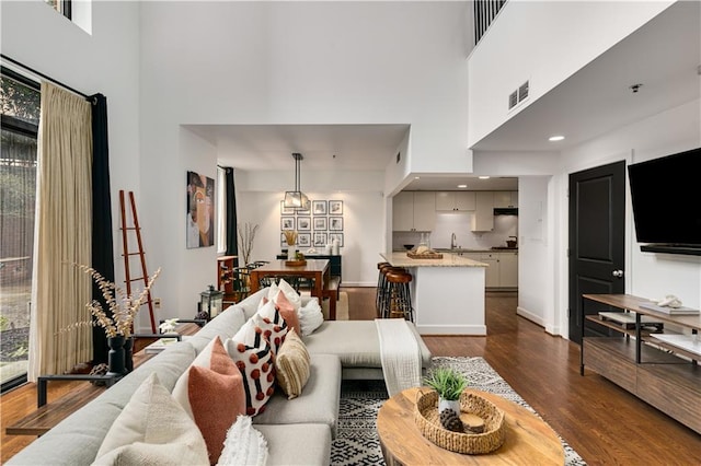 living area featuring visible vents, baseboards, dark wood-style floors, and a towering ceiling