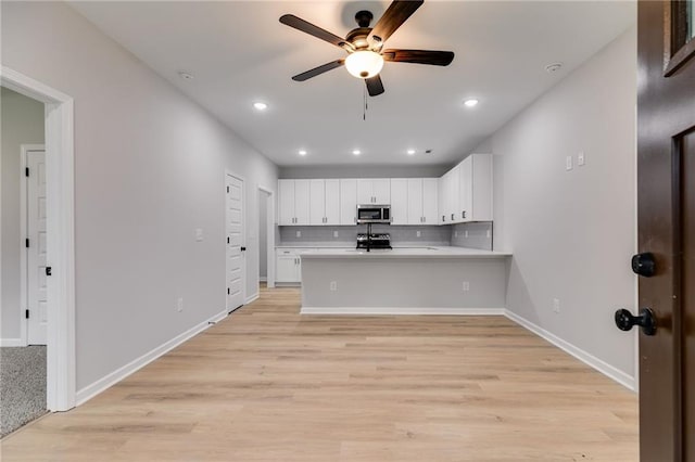 kitchen with tasteful backsplash, range, stainless steel microwave, a peninsula, and light countertops