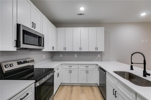 kitchen with light wood-style flooring, stainless steel appliances, a sink, visible vents, and white cabinetry