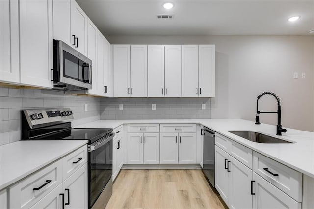 kitchen with light countertops, appliances with stainless steel finishes, white cabinetry, a sink, and light wood-type flooring