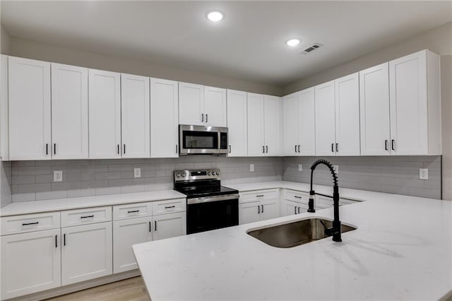 kitchen featuring stainless steel appliances, tasteful backsplash, a sink, and white cabinets