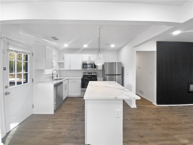 kitchen with sink, appliances with stainless steel finishes, a center island, white cabinets, and decorative light fixtures