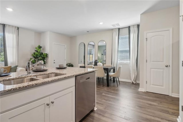 kitchen with open floor plan, light stone countertops, stainless steel dishwasher, white cabinetry, and a sink