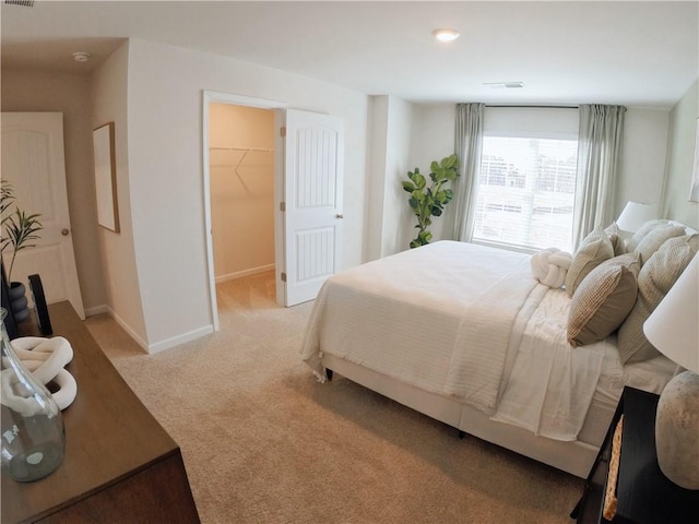 bedroom with baseboards, a walk in closet, visible vents, and light colored carpet