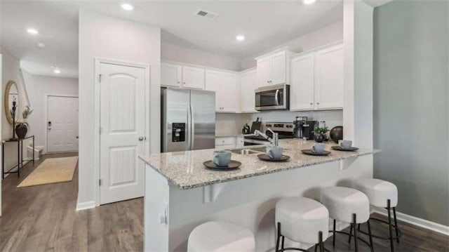 kitchen with a breakfast bar area, stainless steel appliances, a sink, visible vents, and white cabinets