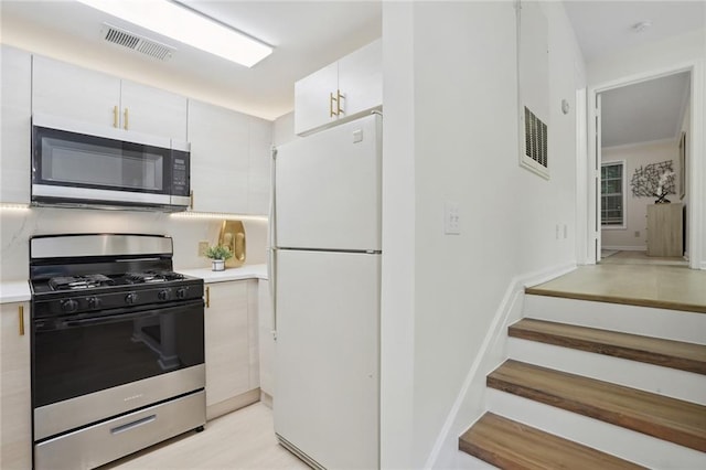 kitchen with light wood-type flooring, white cabinetry, white fridge, and gas range