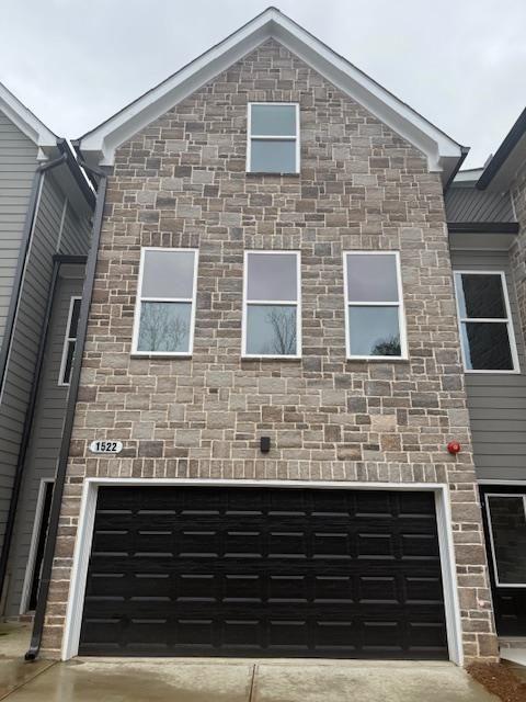 view of front facade with an attached garage, stone siding, and driveway