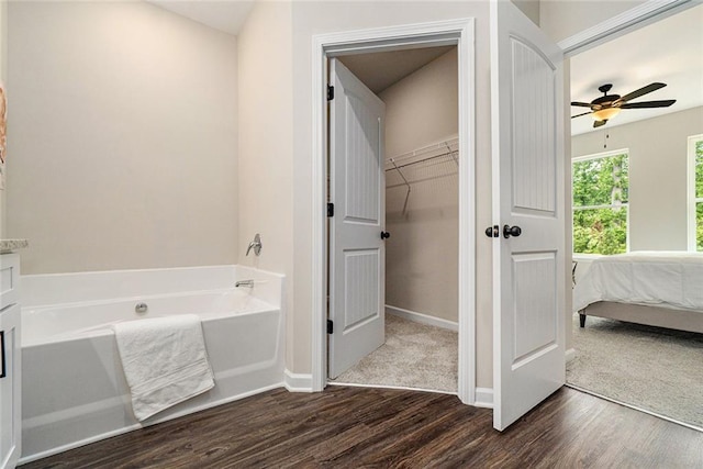 full bathroom featuring a garden tub, a spacious closet, ensuite bathroom, wood finished floors, and baseboards