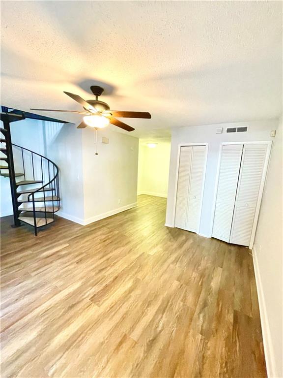 interior space with two closets, a textured ceiling, hardwood / wood-style flooring, and ceiling fan