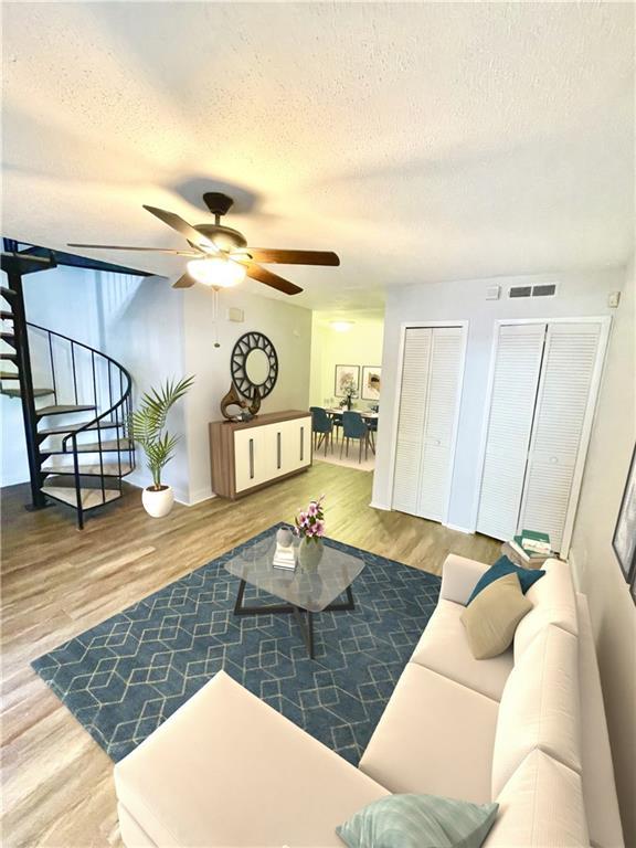 living room with hardwood / wood-style flooring, ceiling fan, and a textured ceiling