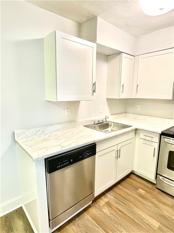 kitchen featuring sink, light wood-type flooring, white cabinets, stainless steel appliances, and a textured ceiling