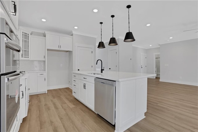 kitchen with an island with sink, glass insert cabinets, appliances with stainless steel finishes, light countertops, and a sink