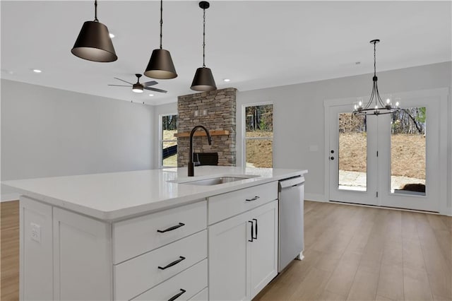 kitchen with light countertops, stainless steel dishwasher, a sink, and a kitchen island with sink