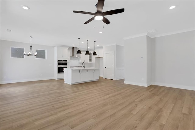 unfurnished living room featuring ceiling fan with notable chandelier, ornamental molding, light wood-style flooring, and recessed lighting