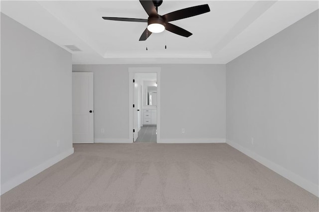 spare room with a tray ceiling, light colored carpet, visible vents, ceiling fan, and baseboards