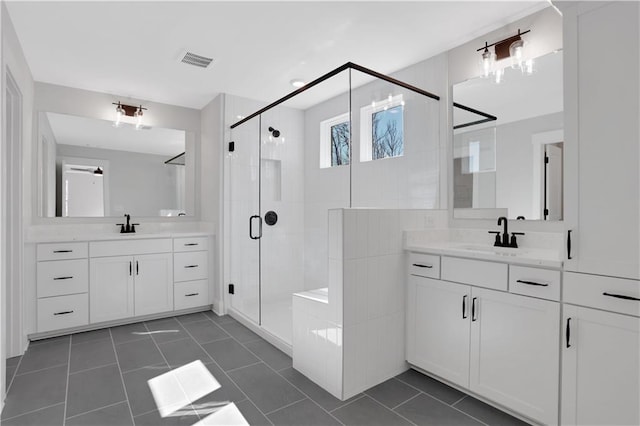 bathroom with two vanities, a stall shower, visible vents, and a sink