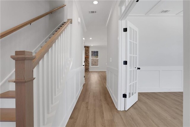 hallway with light wood finished floors, visible vents, a decorative wall, and wainscoting