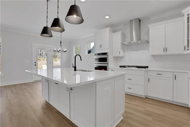 kitchen featuring wall chimney exhaust hood, glass insert cabinets, decorative light fixtures, light countertops, and a sink