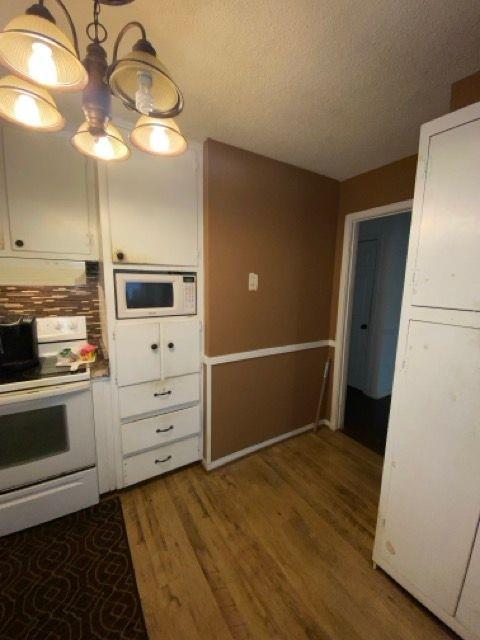 kitchen with hardwood / wood-style floors, white cabinets, range with electric stovetop, and a textured ceiling