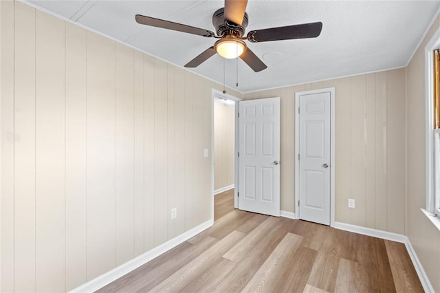 unfurnished bedroom featuring ceiling fan, light wood-type flooring, and wooden walls