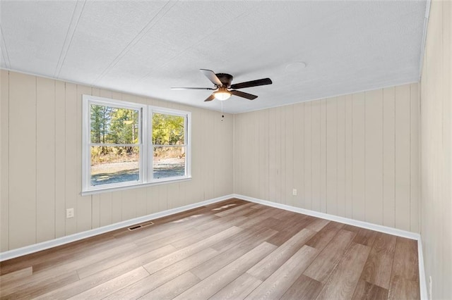 unfurnished room with wooden walls, a textured ceiling, light wood-type flooring, and ceiling fan