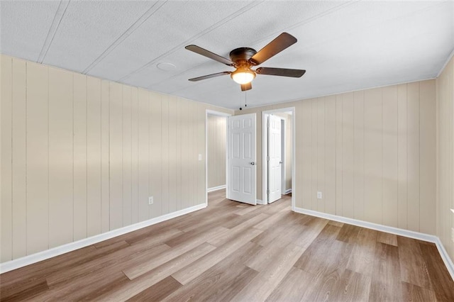 interior space with light hardwood / wood-style flooring, wooden walls, and ceiling fan