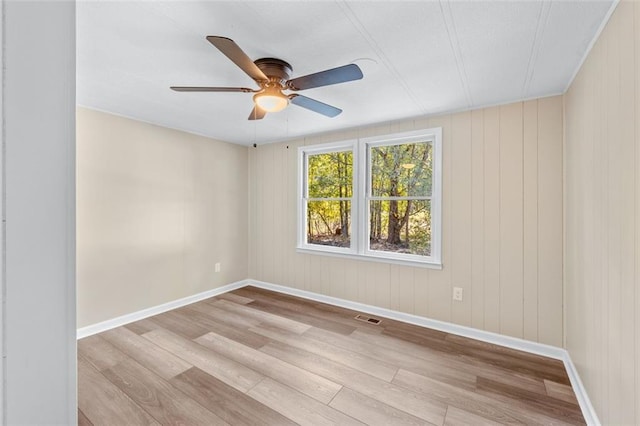 spare room with wooden walls, light wood-type flooring, and ceiling fan