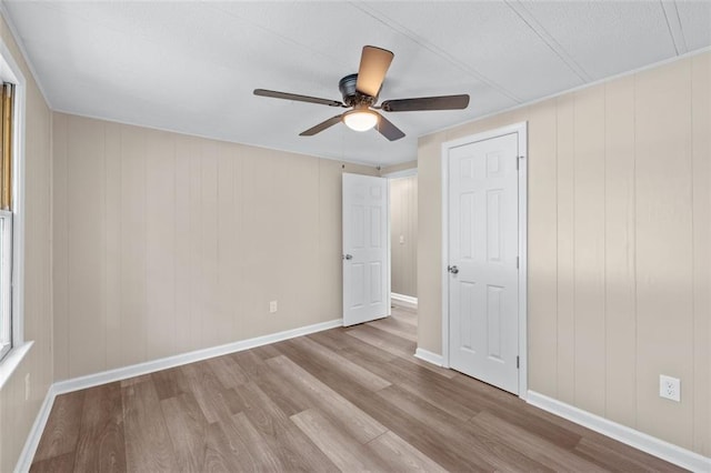 unfurnished bedroom with ceiling fan, wood walls, and light wood-type flooring