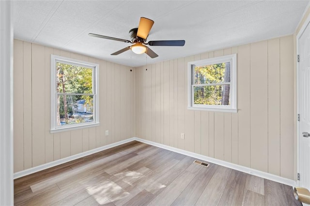 unfurnished room featuring wood walls, a healthy amount of sunlight, light wood-type flooring, and ceiling fan