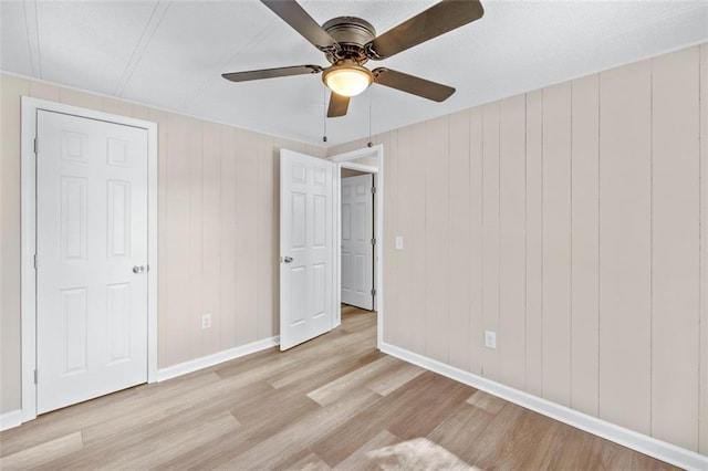 unfurnished bedroom featuring wooden walls, light hardwood / wood-style floors, and ceiling fan