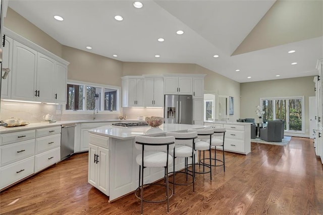 kitchen featuring a center island, appliances with stainless steel finishes, white cabinetry, wood finished floors, and a kitchen bar