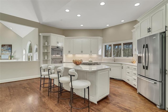 kitchen with dark wood finished floors, appliances with stainless steel finishes, a kitchen breakfast bar, a center island, and light countertops