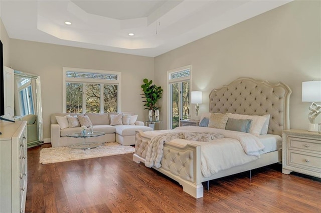 bedroom featuring dark wood-style floors, a tray ceiling, and multiple windows